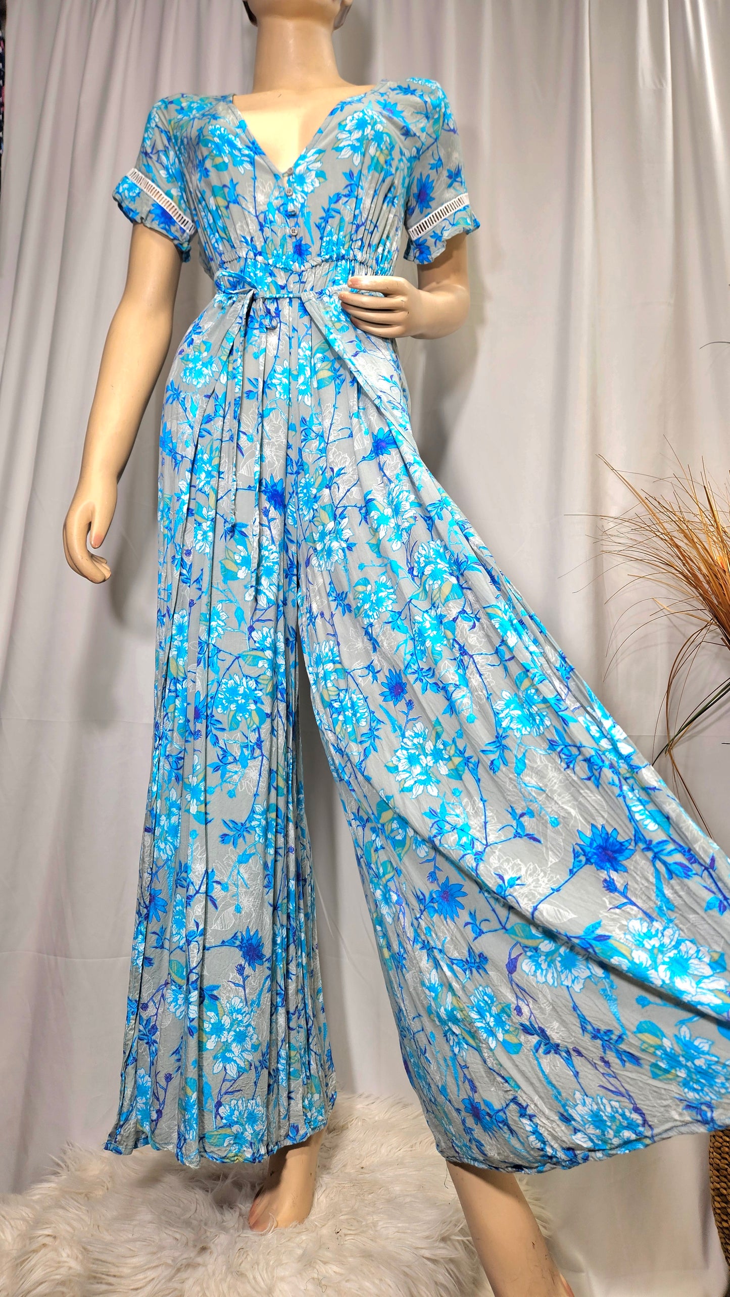 A model wearing a floral jumpsuit with wide legs and lace details on the sleeves, in blue and white colors. in good preloved condition in auckland based size small - medium