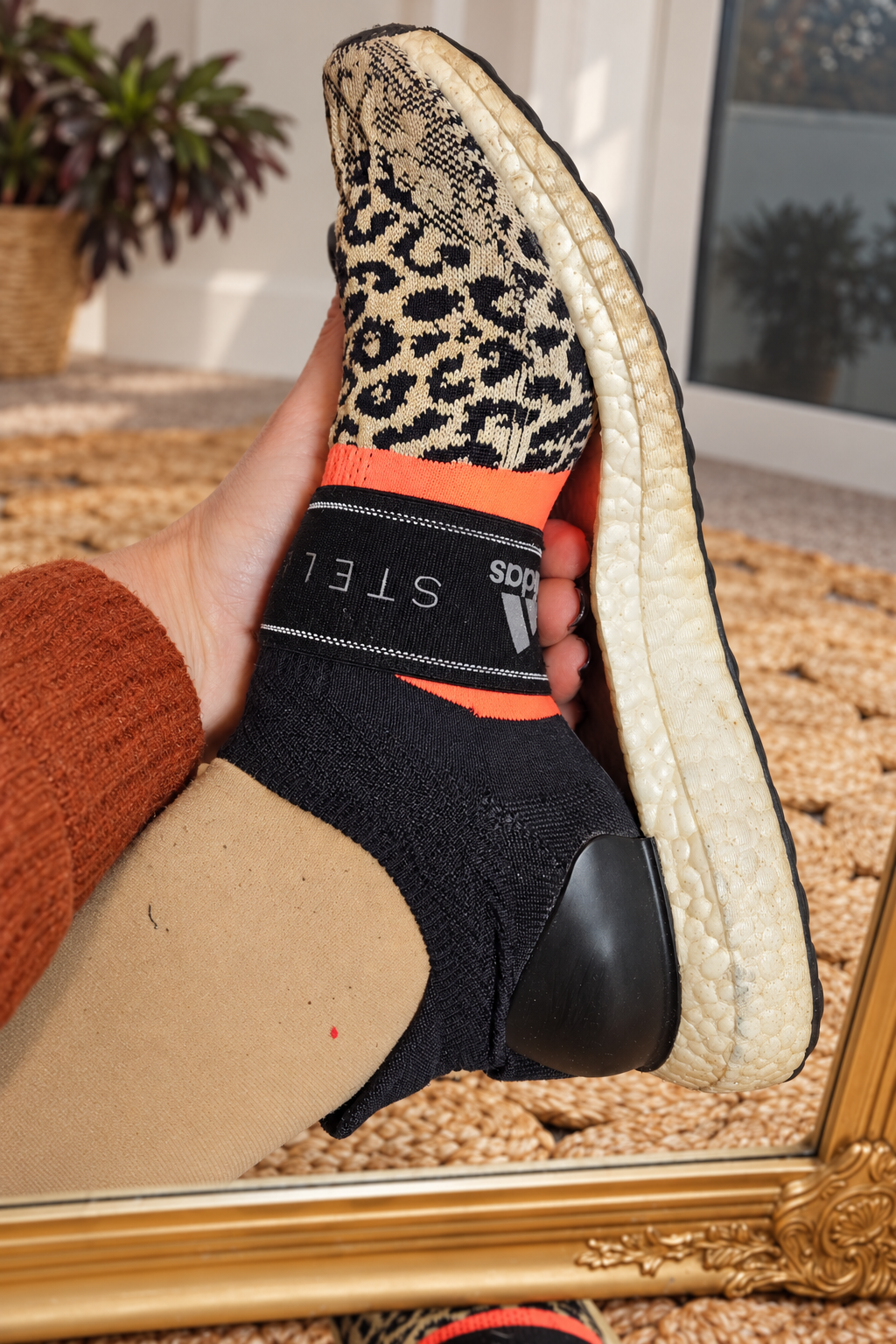 Side view of Adidas Stella McCartney leopard knit sneakers showing black sock-style upper, coral details and white UltraBoost sole.